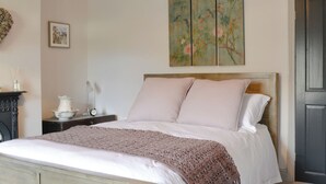 Un dormitorio con cama, mesita de noche, lámpara, un cuadro y una puerta.