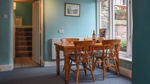 Un coin repas avec une table et des chaises en bois, un tableau encadré au mur et une fenêtre donnant sur l’extérieur.