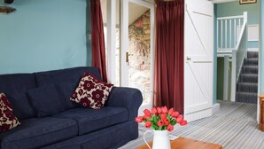 Un salon avec un canapé bleu foncé, des rideaux rouges, un vase blanc contenant des fleurs rouges et une table basse en bois.