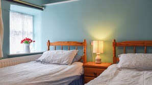 Une chambre avec deux lits simples, une table de chevet avec une lampe, une fenêtre donnant sur un beau paysage et un vase rempli de fleurs.