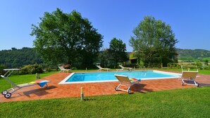 Una piscina rectangular con borde de baldosas, rodeada de césped verde y árboles.