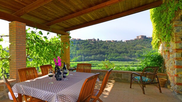 Un patio al aire libre con una mesa dispuesta para comer, rodeado de pilares de ladrillo y sillas de madera.