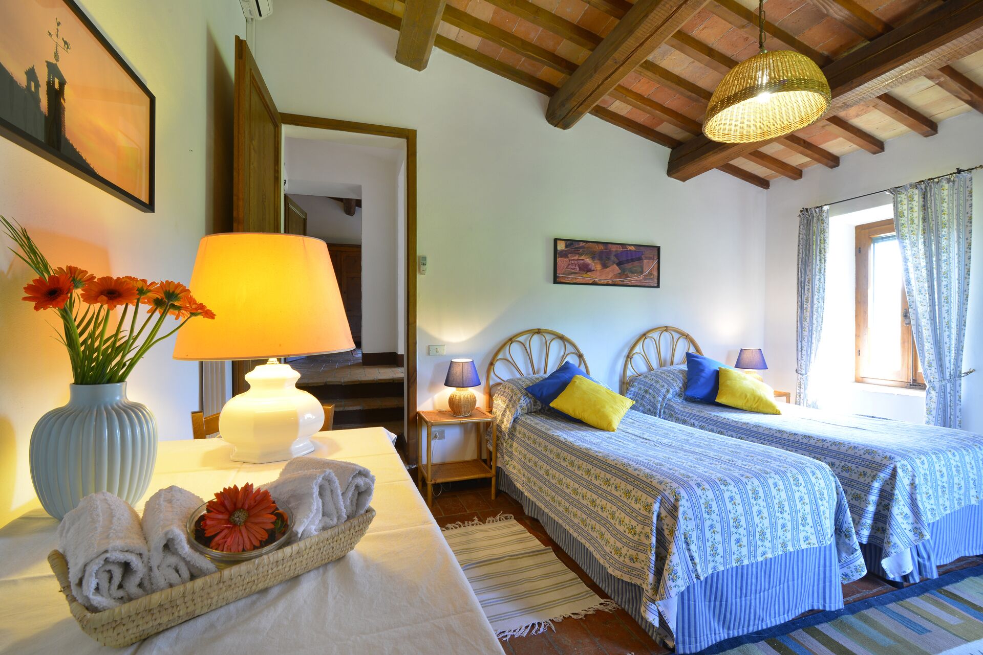 Un dormitorio acogedor con dos camas, techo de madera, un cuadro y una ventana con cortinas.