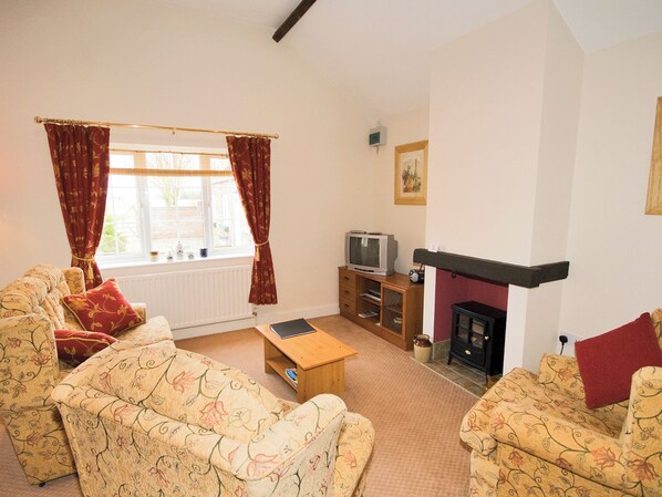 A living room with floral-patterned sofas, a wooden coffee table, a fireplace, and a television on a wooden stand. - Mallard Cottage - E3751 (Leverton)