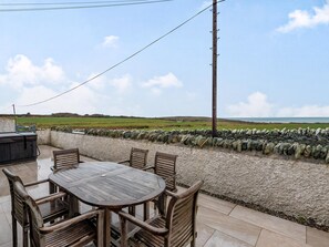 A patio with a wooden table and chairs, a stone wall, and a view of the countryside. - 3 bedroom accommodation in Penrhos Feilw, near Trearddur Bay (Penrhos Feilw, near Trearddur Bay)