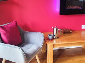 Une pièce avec un canapé gris, une table en bois, une cafetière, une tasse et une petite boîte en bois.