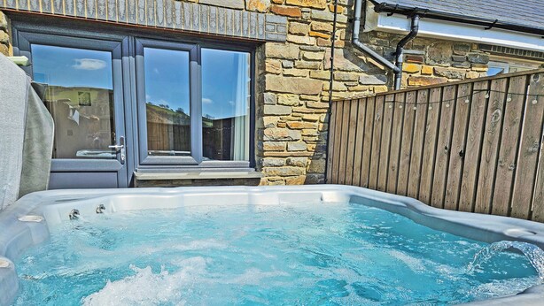 A hot tub in a backyard with stone walls and a wooden fence. - 3 bedroom accommodation in Dihewyd, near Aberaeron (Dihewyd, near Aberaeron)