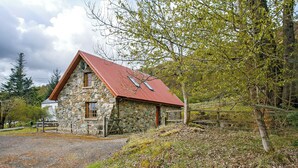 Um edifício de pedra com telhado vermelho, rodeado por árvores e um caminho de cascalho.
