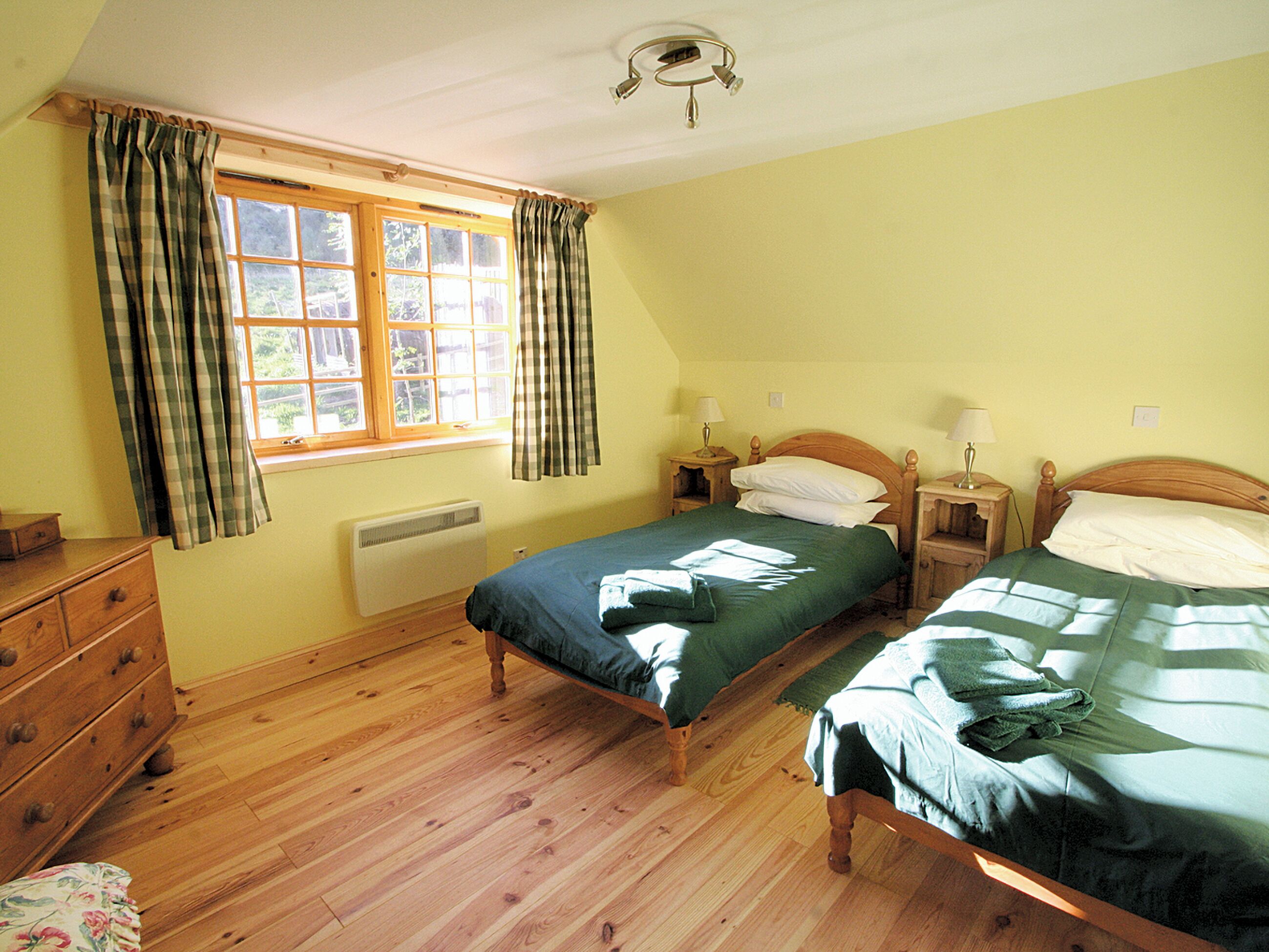 A bedroom with two single beds, a wooden dresser, a window with curtains, and a ceiling light fixture.