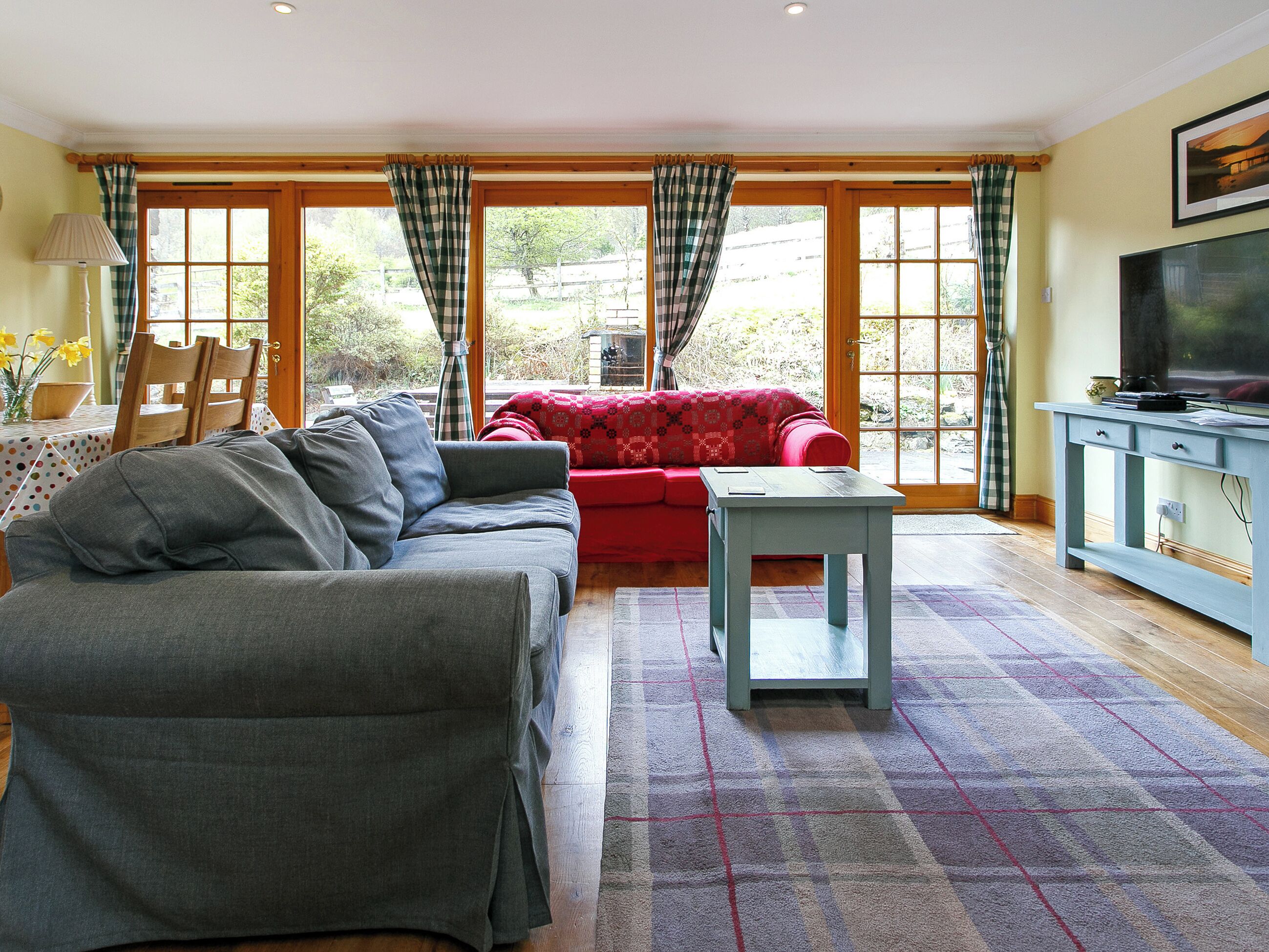 A living room with a grey sofa, a red sofa, a small table, and a TV on a blue cabinet.