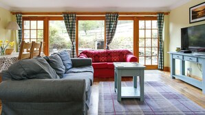Uma sala de estar com um sofá cinzento, um sofá vermelho, uma mesinha e uma televisão sobre um móvel azul.