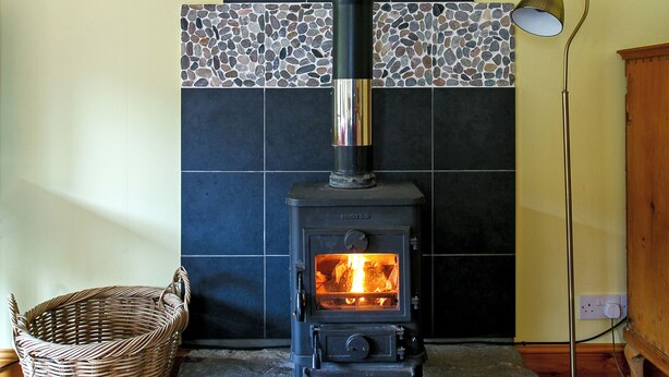 A wood-burning stove with a tiled wall behind it.