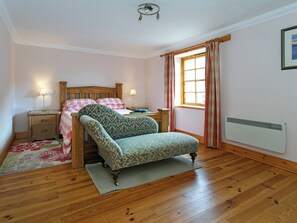 Un dormitorio con una cama de madera, una silla, una mesita de noche, una lámpara, una ventana con cortinas y un radiador.