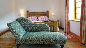 Um quarto com cama de madeira, poltrona estampada e janela com cortinas.