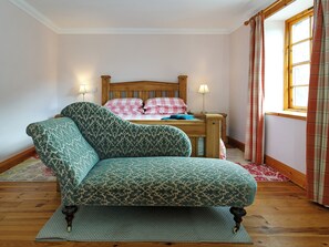 A bedroom with a wooden bed, a patterned armchair, and a window with curtains.