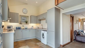 A modern kitchen with grey cabinets, a microwave, a washing machine, and a clock on the wall. - 4 bedroom accommodation in Beck Hole, near Goathland (Beck Hole, near Goathland)