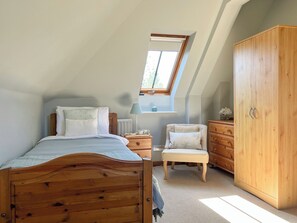 A bedroom with a sloped ceiling, a wooden bed, a chair, a dresser, and a window.