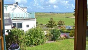 A white building with a balcony, surrounded by green fields and a clear sky. - 2 bedroom accommodation in Llanfairynghornwy (Llanfairynghornwy)