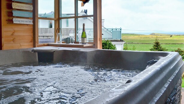 A hot tub in a wooden cabin with a view of a green landscape. - 2 bedroom accommodation in Llanfairynghornwy (Llanfairynghornwy)