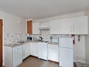 A compact kitchen with white cabinets, a microwave, a stove, and a refrigerator. - Pear Tree Farm Cottages - RCHM38 (Ebberston, near Scarborough)