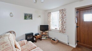 A living room with a sofa, television, fireplace, and a wooden door. - Pear Tree Farm Cottages - RCHM38 (Ebberston, near Scarborough)