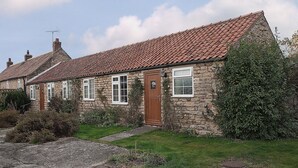 A stone house with a tiled roof, a wooden door, and a small garden. - Pear Tree Farm Cottages - RCHM38 (Ebberston, near Scarborough)