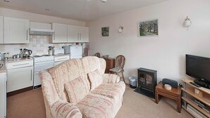 A living room with a sofa, a television, a fireplace, and a kitchen area with cabinets and appliances. - Pear Tree Farm Cottages - RCHM38 (Ebberston, near Scarborough)