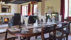 A dining room with a wooden table set for four, surrounded by upholstered chairs. A fireplace is visible in the background, and the room has a traditional architectural style with exposed wooden beams on the ceiling. - Kiln Green Farmhouse (Near Milnthorpe)