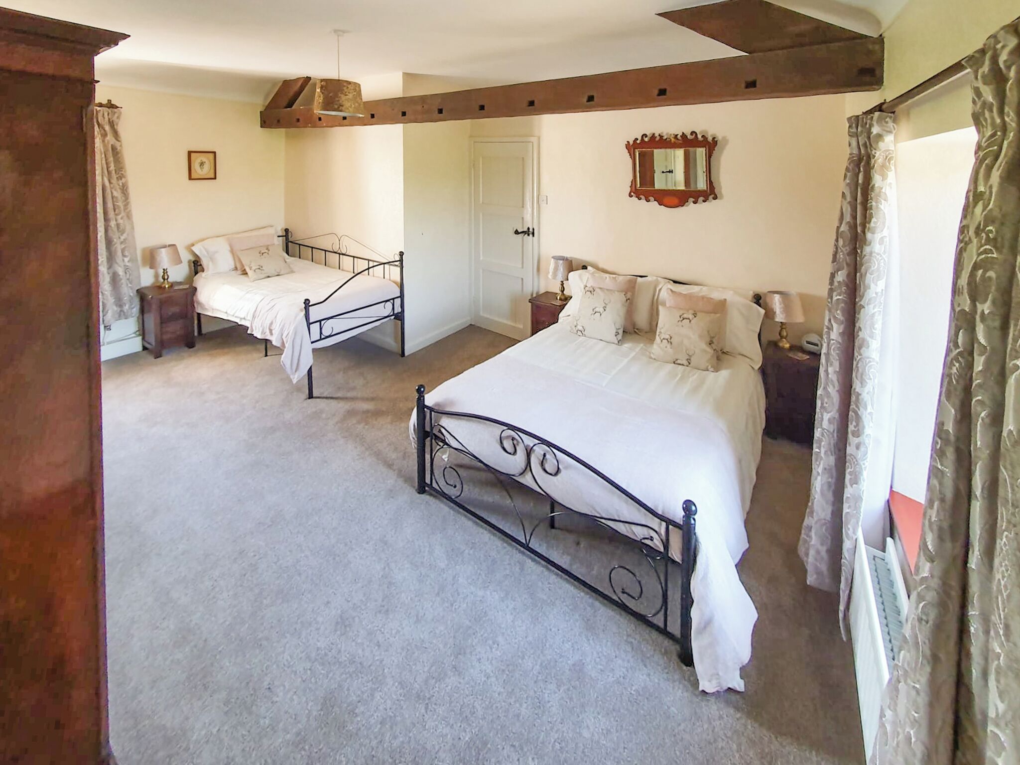 A bedroom with two beds, a door, a mirror, and a small table with a lamp.