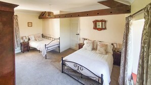A bedroom with two beds, a door, a mirror, and a small table with a lamp. - Kiln Green Farmhouse (Near Milnthorpe)