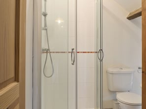 A glass-enclosed shower with a handheld showerhead, a toilet, and a tiled wall with a decorative border. - 3 bedroom accommodation in Catfield (Catfield)