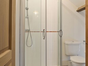 A glass-enclosed shower with a handheld showerhead, a toilet, and a tiled wall with a decorative border.