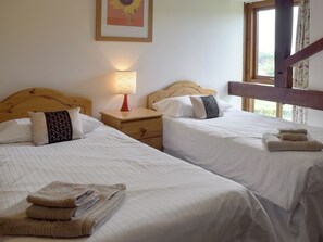 A hotel room with two beds, each with white linens and a wooden headboard. There is a nightstand with a lamp between the beds, and a framed picture of a sunflower on the wall.
