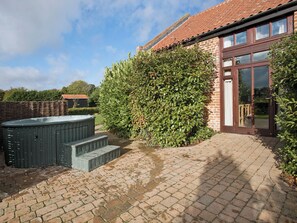 A brick house with a large hedge, a hot tub, and a paved patio.