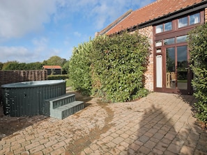 A brick house with a large hedge, a hot tub, and a paved patio. - 3 bedroom accommodation in Catfield (Catfield)