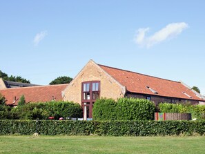 A brick building with a red-tiled roof, a prominent entrance with a glass door, and a well-maintained hedge in front.