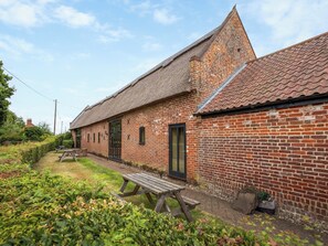 Een gebouw van baksteen met rieten dak, een houten bankje en een tuin.