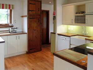 A kitchen with wooden cabinets, a dishwasher, a toaster, and a window with a striped valance.