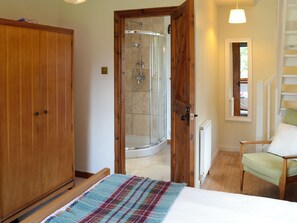 A bedroom with a bed, a wooden wardrobe, a shower area, and a chair.