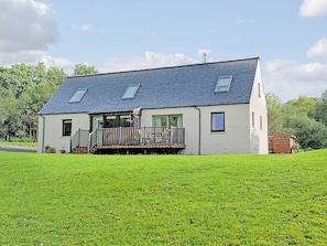 A two-story house with a sloped roof, a balcony, and a grassy yard. - Allt Beag (Little Streams) (Achintraid, near Lochcarron)