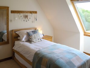 A bedroom with a wooden bed, a nightstand, a wall-mounted star decoration, and a window with a view of greenery. - Allt Beag (Little Streams) (Achintraid, near Lochcarron)
