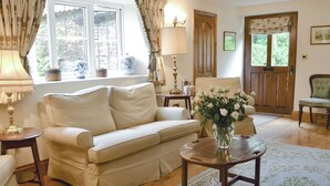 Un salon chaleureux avec un canapé, une table ornée d’un vase de fleurs, une lampe et une porte en bois.