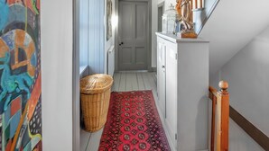 A hallway with a patterned rug, a wicker basket, a door, and a staircase with a wooden handrail. - 5 bedroom accommodation in Lochinver (Lochinver)