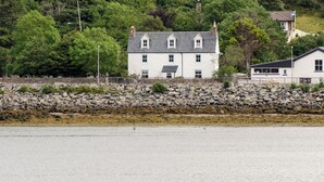 A coastal building with a white facade, multiple windows, and a stone wall in the foreground. - 5 bedroom accommodation in Lochinver (Lochinver)