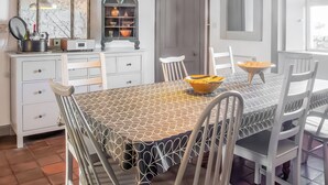 A dining area with a patterned tablecloth, white chairs, a bowl on the table, a pendant light, and a vintage-style mirror. - 5 bedroom accommodation in Lochinver (Lochinver)