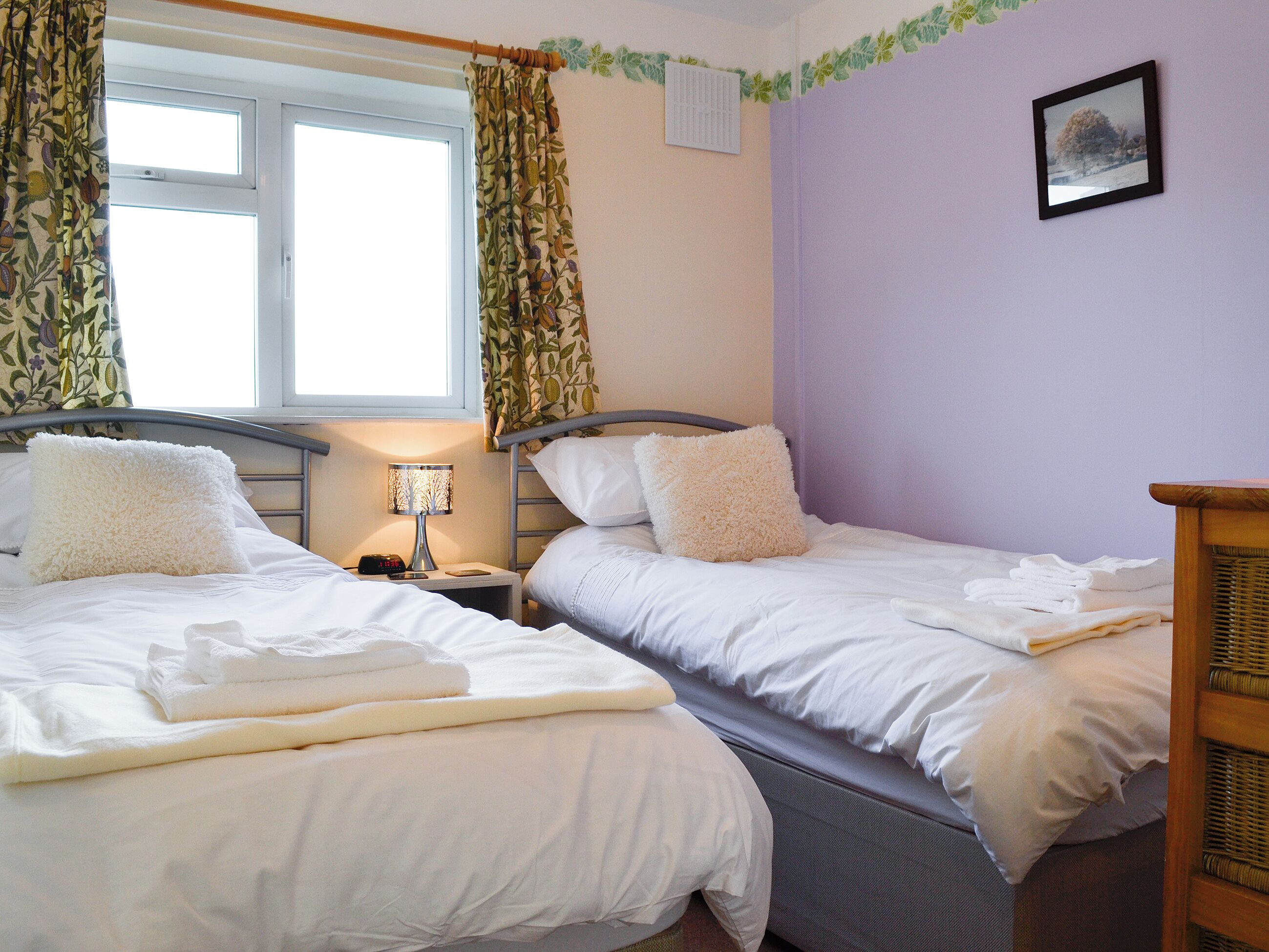 Habitación doble con dos camas, una ventana con cortinas, una mesita de noche con lámpara y un cuadro en la pared.