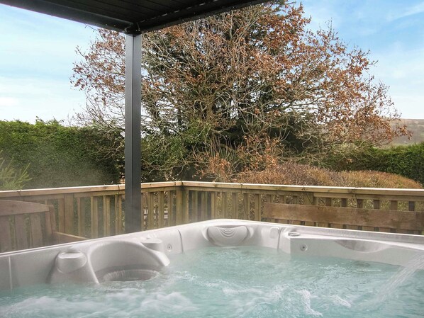 Un bain à remous doté d’une terrasse en bois et d’un toit en métal, entouré d’arbres et d’arbustes.