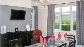 Ein Esszimmer mit Kamin, einem an der Wand montierten Fernseher und Blick ins Freie durch das Fenster.