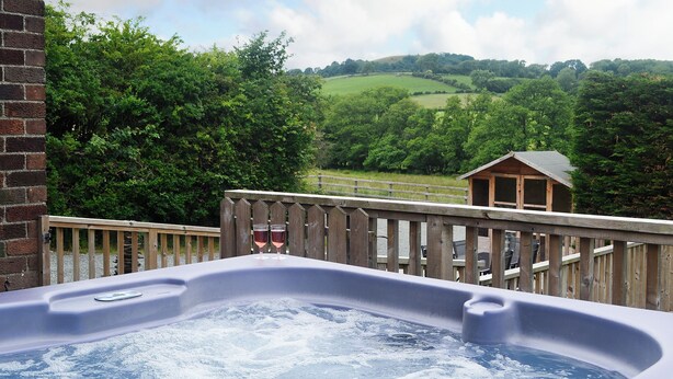 Ein Whirlpool mit zwei Weingläsern auf einer Holzterrasse mit Blick auf eine grüne Landschaft.