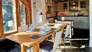 A dining area with a wooden table set for four, a kitchen in the background, and a view of greenery outside. - 2 bedroom accommodation in Burpham, near Arundel (Burpham, near Arundel)